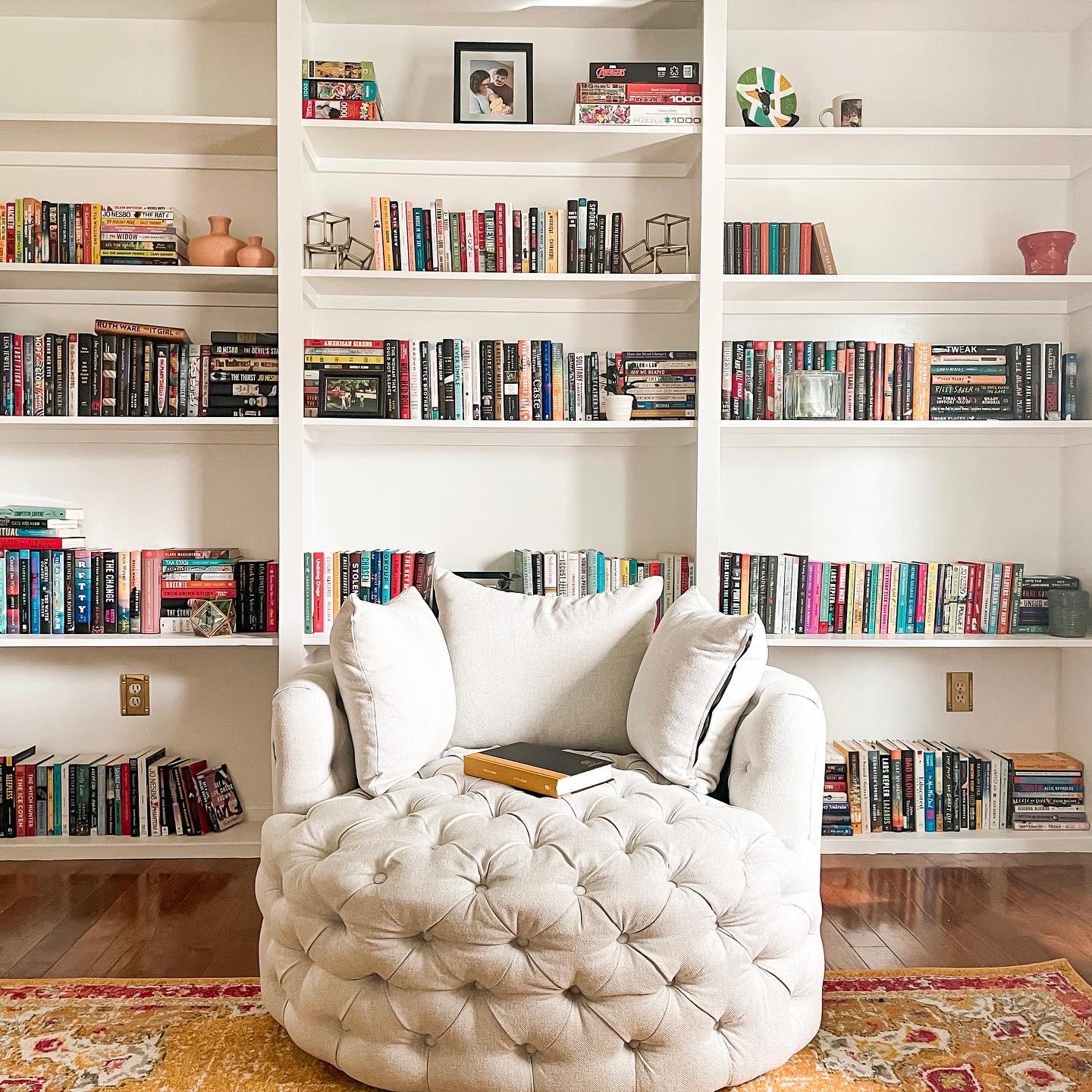 a large white, round reading chair sitting in front of floor-to-ceiling white bookshelves.