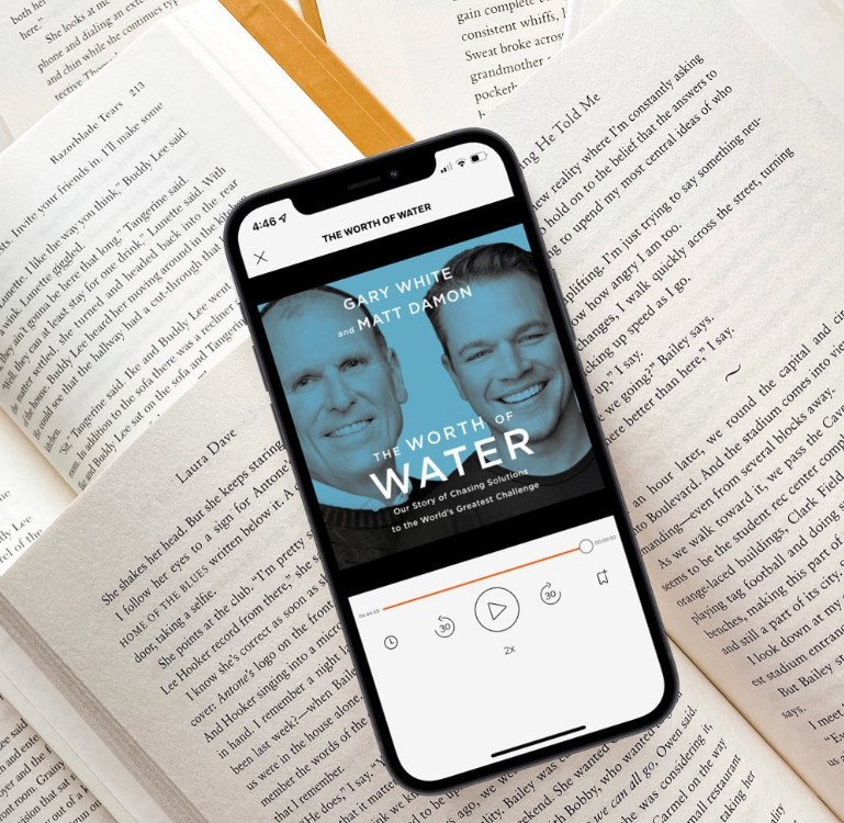 The Worth of Water audiobook on a cell phone, sitting on a pile of open books